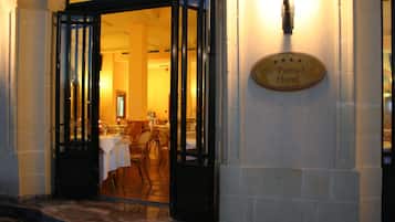 La entrada al Hotel St. Patrick con un cartel sobre la puerta, un área de comedor visible en el interior y una pared de piedra a la derecha.