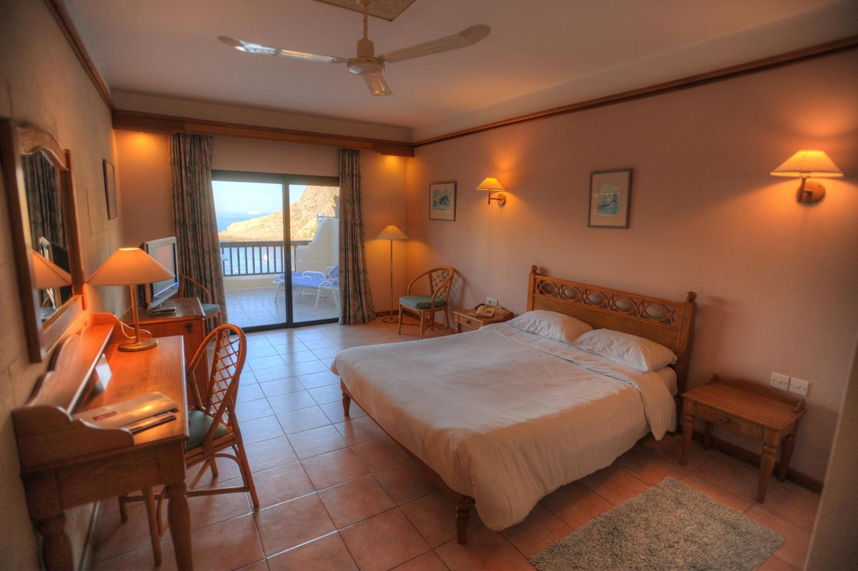 Habitación de hotel con cama, escritorio, silla y balcón con vistas.