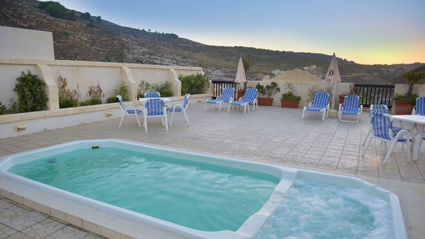Uma área de piscina no terraço com espreguiçadeiras e uma banheira de hidromassagem, cercada por plantas em vasos e com vista para uma paisagem montanhosa.