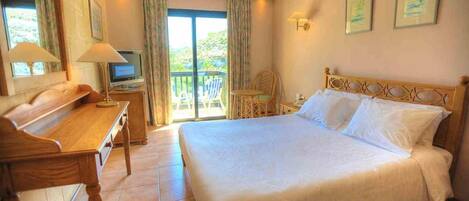 A hotel room with a bed, a desk, a television, and a balcony with chairs.