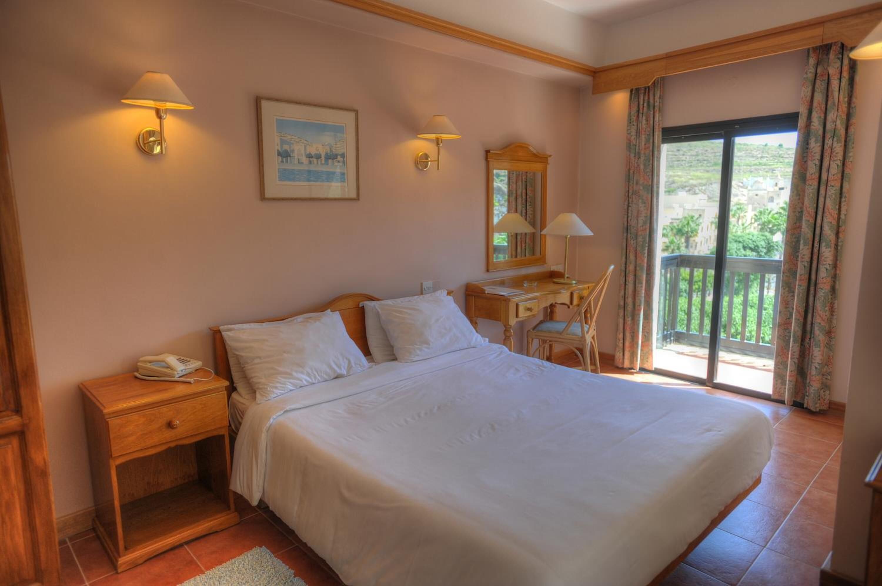 A bedroom with a large bed, bedside tables, a desk, and a balcony with curtains.