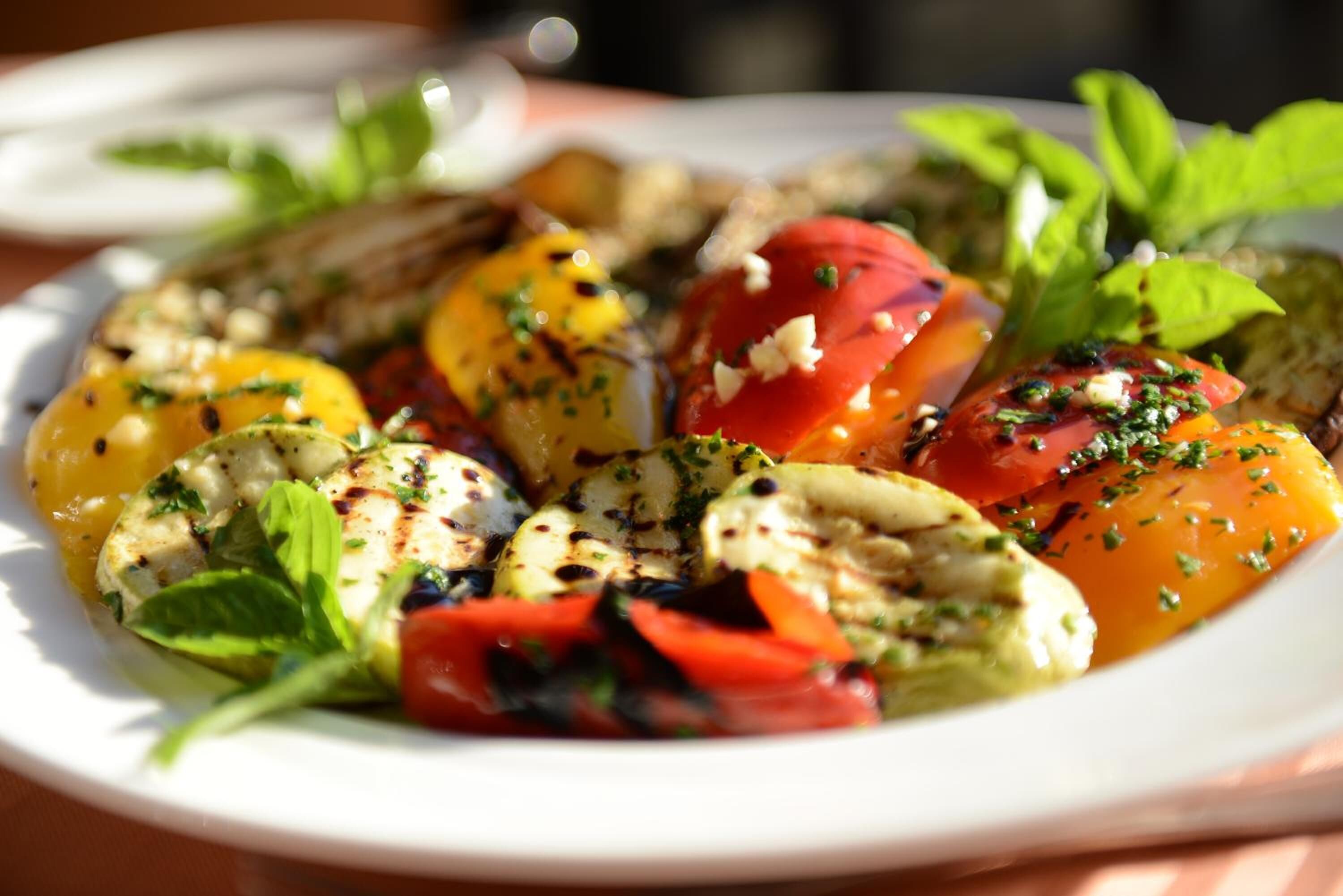 Un plato de pollo a la parrilla, tomates y hojas verdes.
