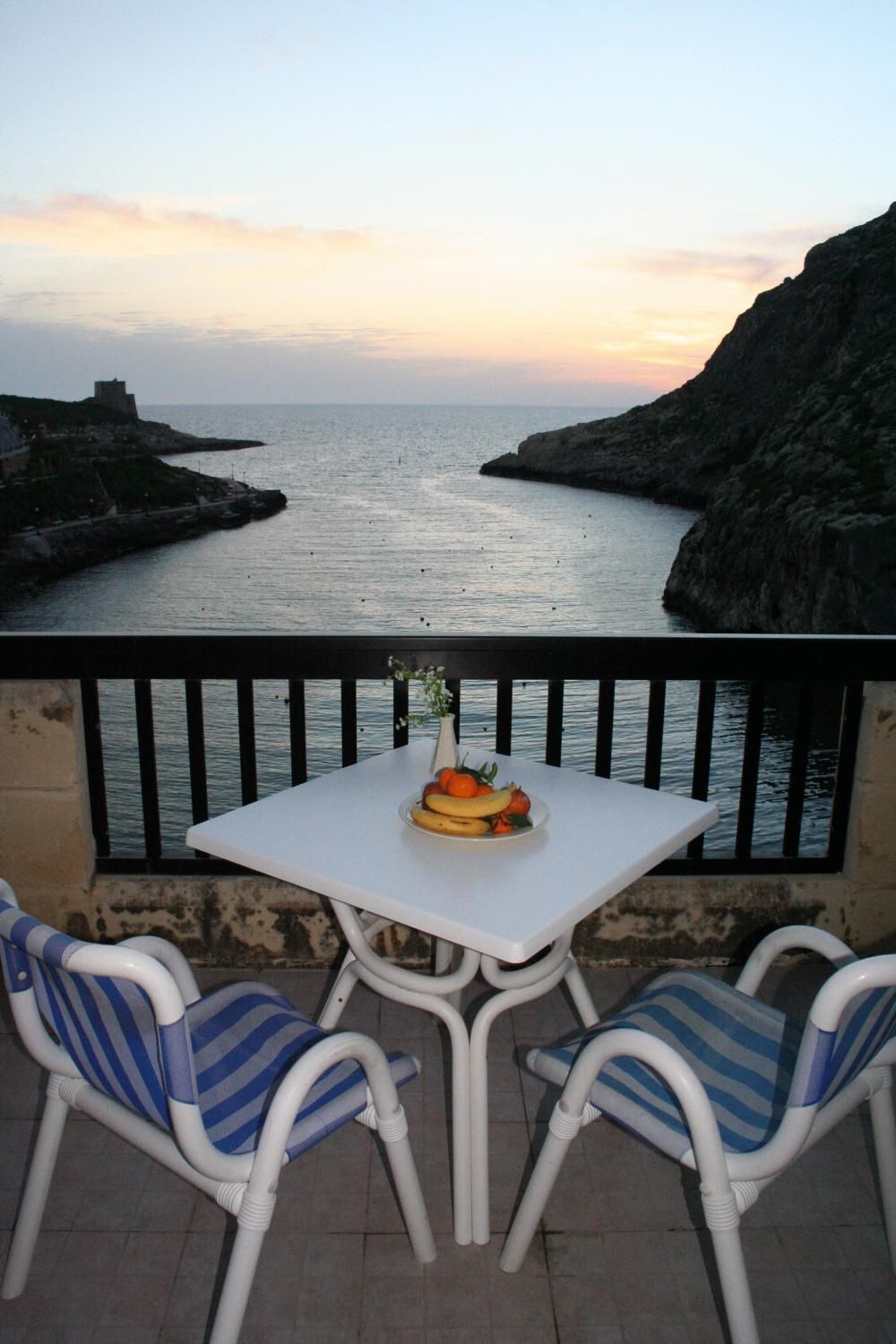 Un balcón con una mesa y dos sillas, con vistas a un paisaje costero con acantilados y el mar.