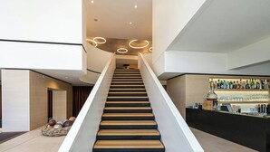 A modern interior with a central staircase, a bar area with shelves of bottles, and a minimalist design. - Stadthotel Münster (Münster)