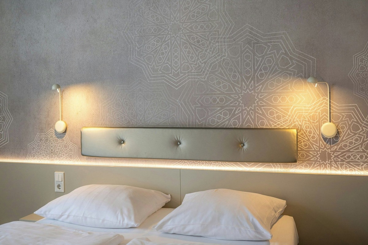A bed with two pillows, a headboard with a light fixture, and a patterned wall.