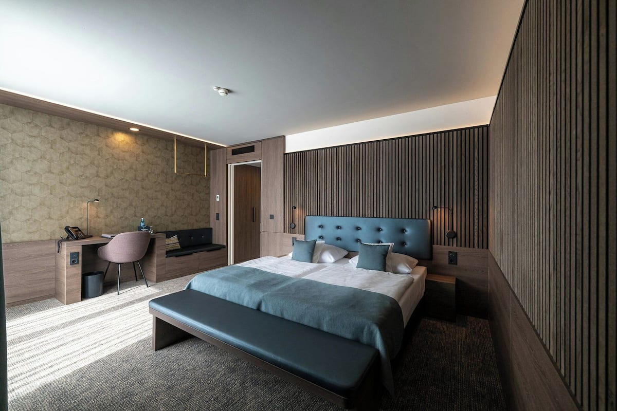 A modern hotel room with a large bed, a desk, a chair, and a bench.