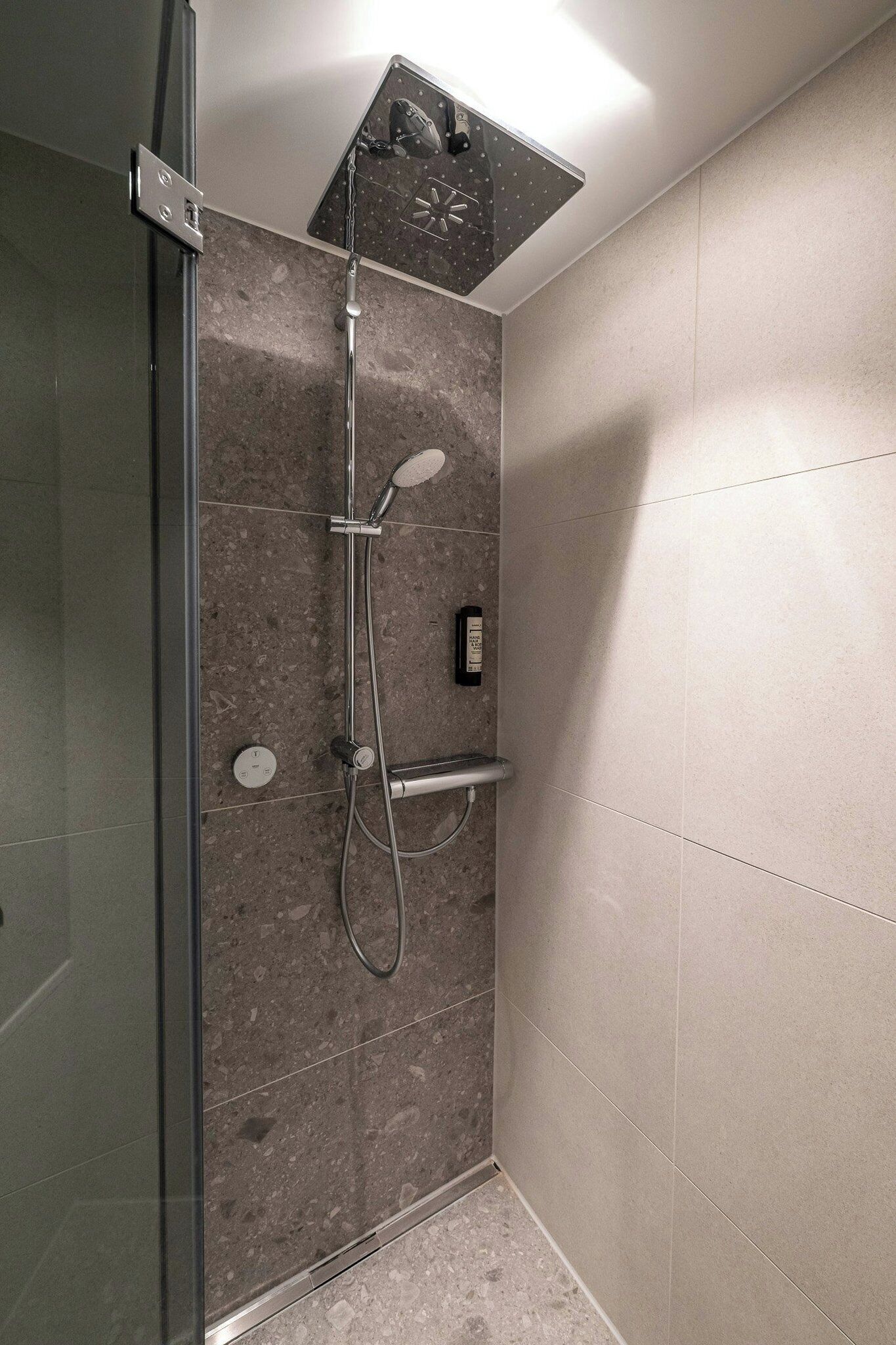 Eine Dusche mit Handbrause, einer fest installierten Bedienung und einer Glasduschwand.