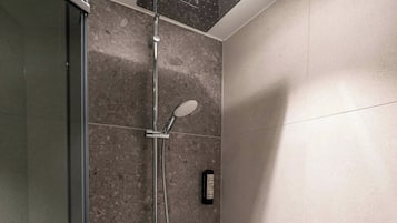 Eine Dusche mit Handbrause, einer fest installierten Bedienung und einer Glasduschwand.
