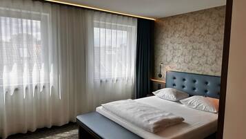 A hotel room with a bed, a bench, a window with curtains, and a patterned wall.