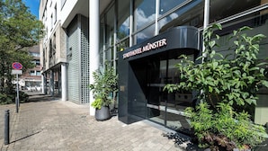 A hotel entrance with a sign reading 'Stadthotel Munster,' potted plants, and a paved walkway. - Stadthotel Münster (Münster)
