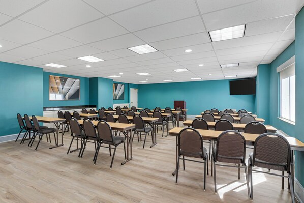 Un salón de conferencias con paredes color turquesa, mesas y sillas de madera dispuestas para una reunión.