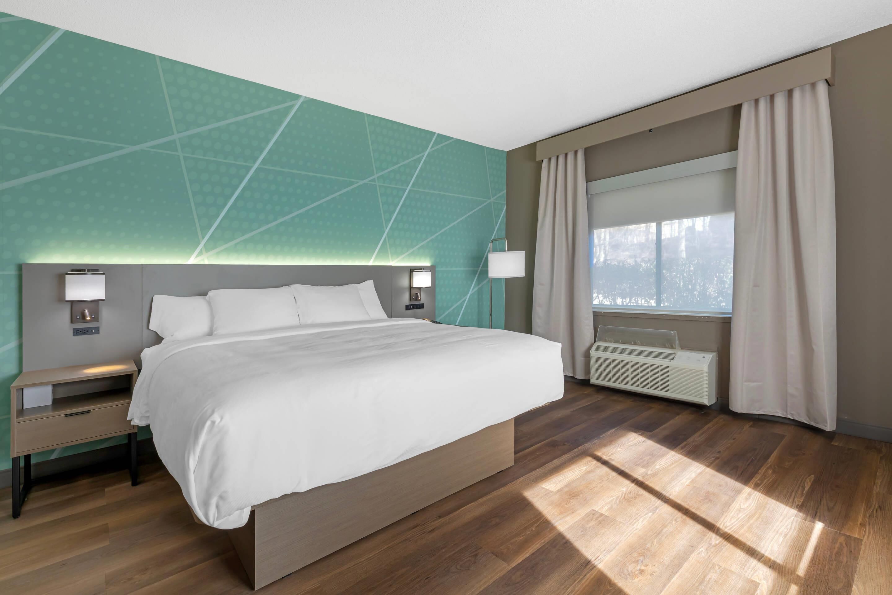 Une chambre d’hôtel moderne avec un grand lit, des tables de chevet avec des lampes, une fenêtre avec des rideaux et un radiateur.
