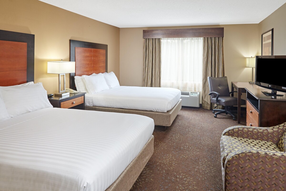 A hotel room with two beds, a desk, a chair, a television, and a window with curtains.
