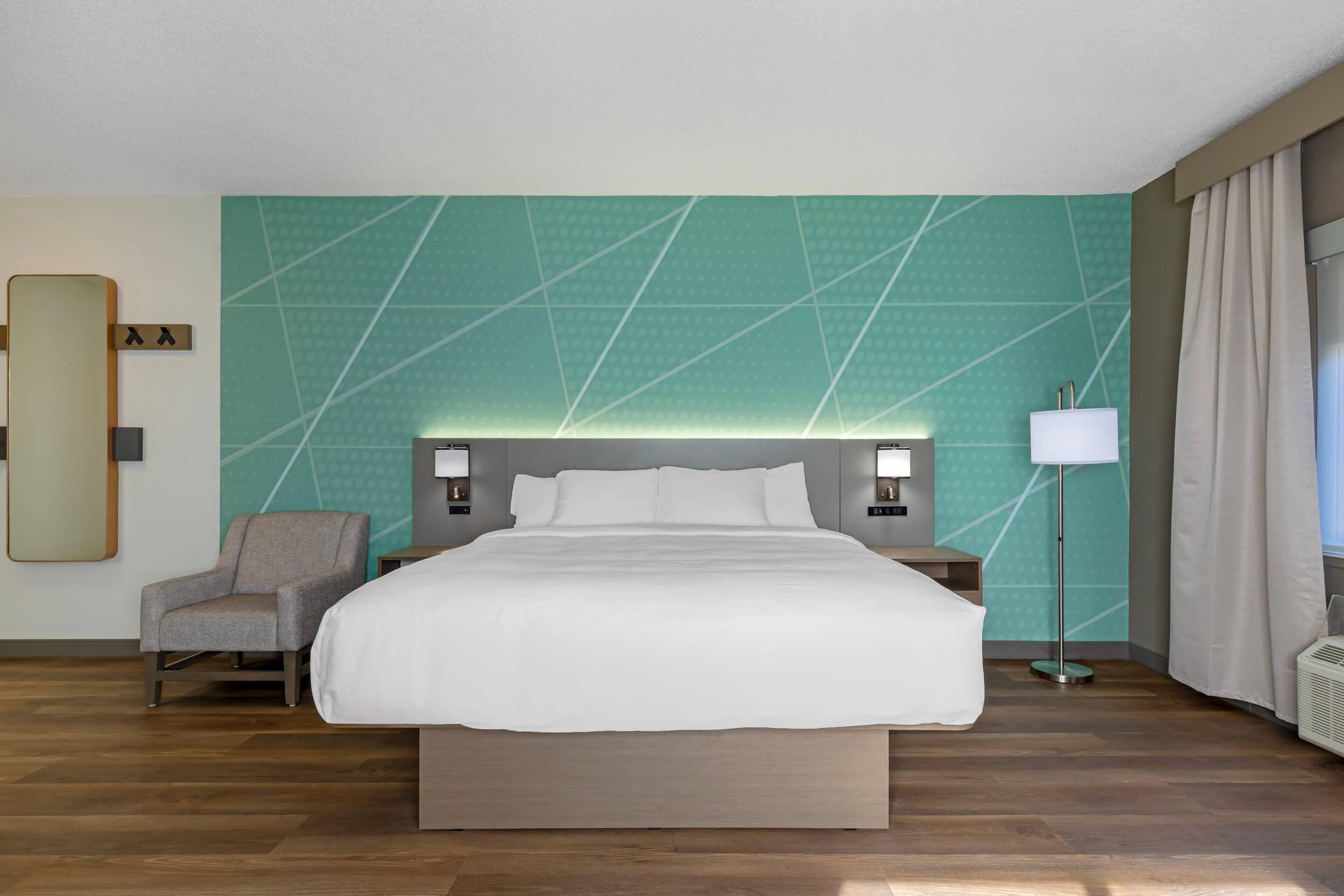 A hotel room with a large bed, a chair, a nightstand, a lamp, and a mirror.