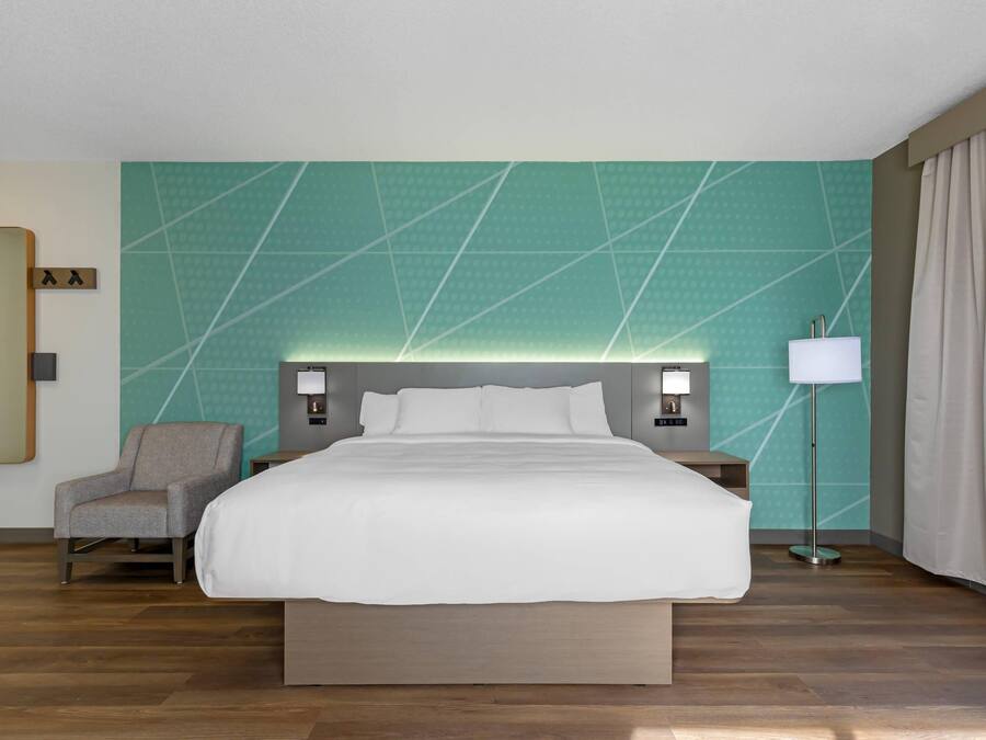 A hotel room with a large bed, a chair, a nightstand, a lamp, and a mirror.