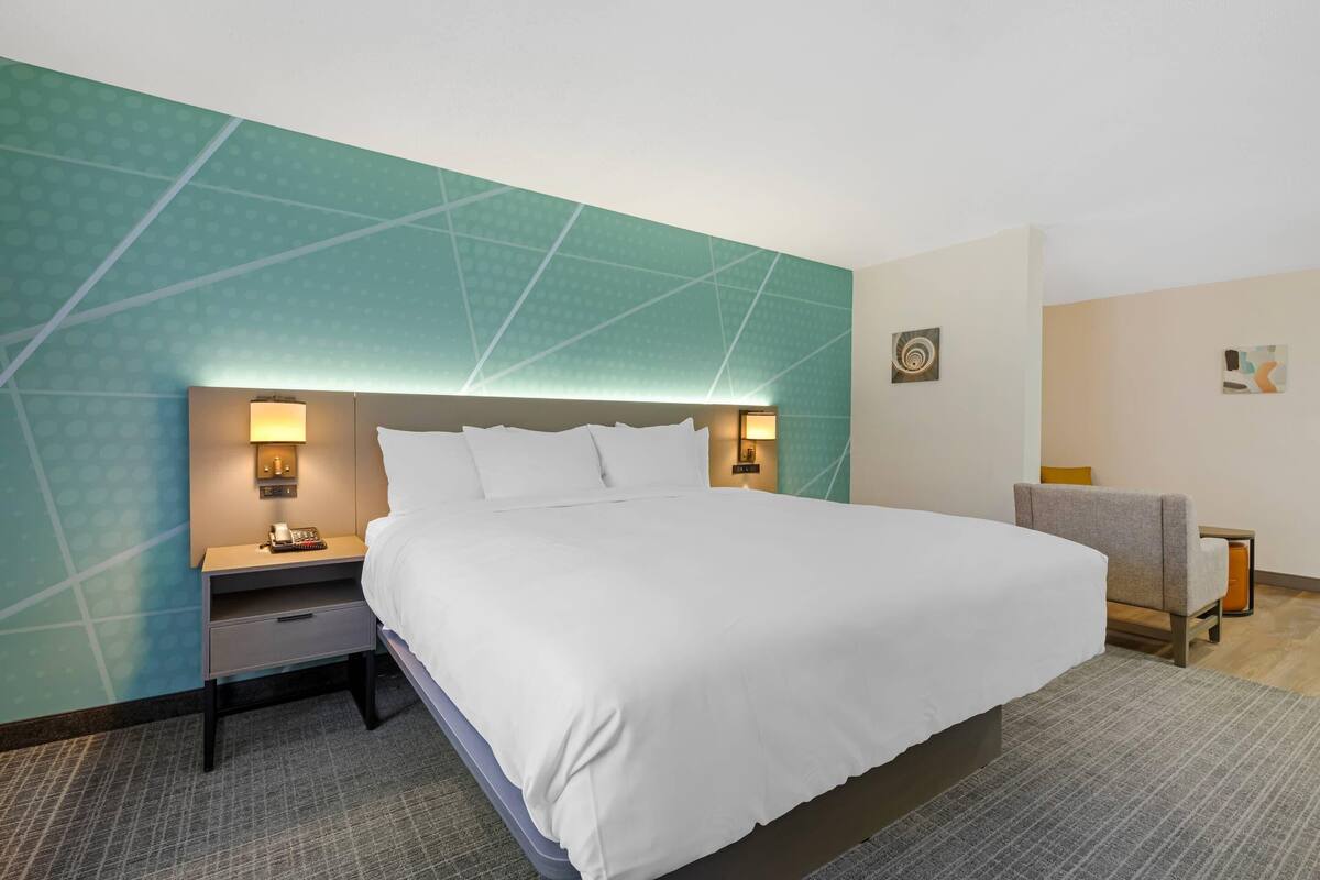 Habitación de hotel con una cama grande, dos mesitas de noche con lámparas, una silla y una pared con un diseño geométrico.