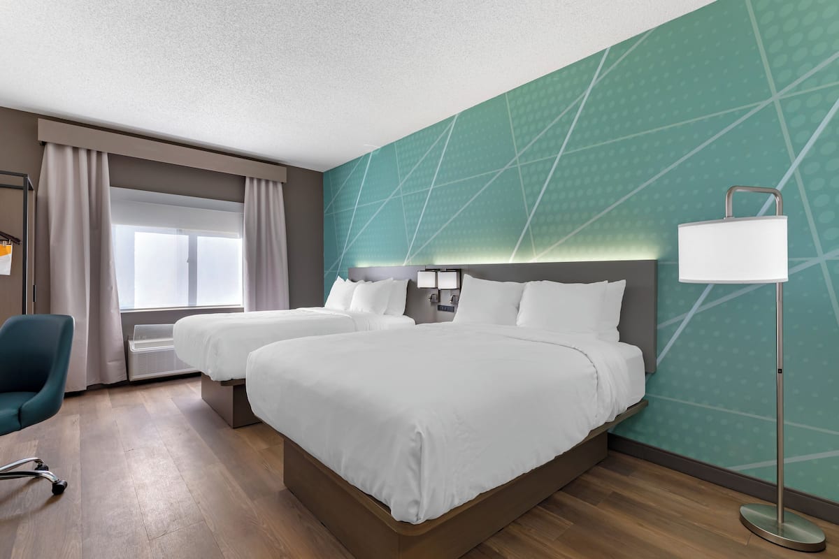 Habitación de hotel con dos camas, un escritorio, una silla y un ventanal con cortinas.
