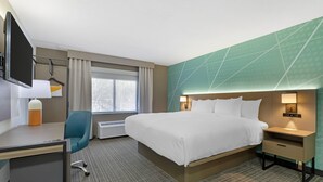 Ein Hotelzimmer mit Bett, Schreibtisch, Stuhl, Fernseher und einem Fenster mit Vorhängen.