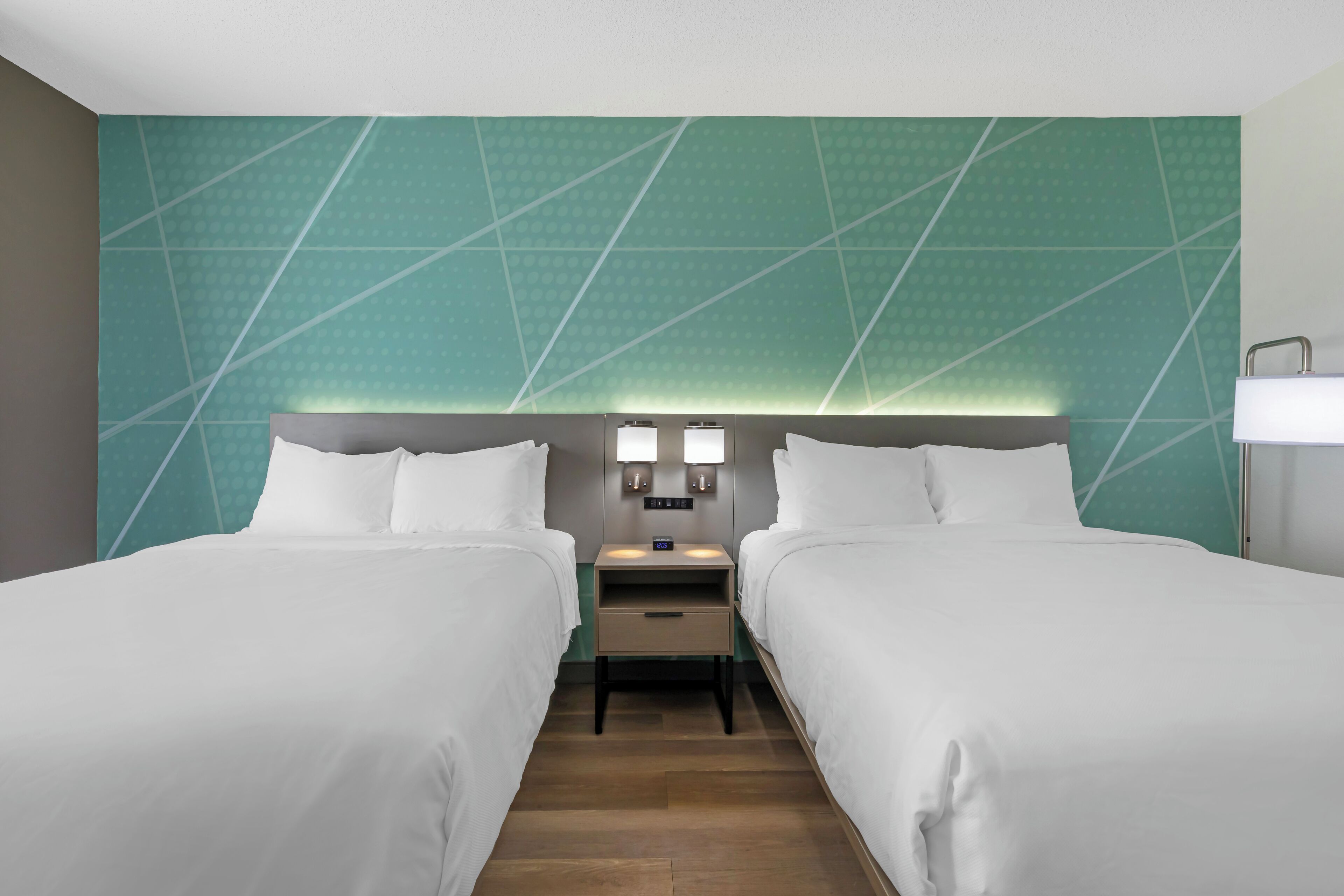 Hotelkamer met twee bedden, een nachtkastje met een lamp en een muur met een geometrisch patroon.