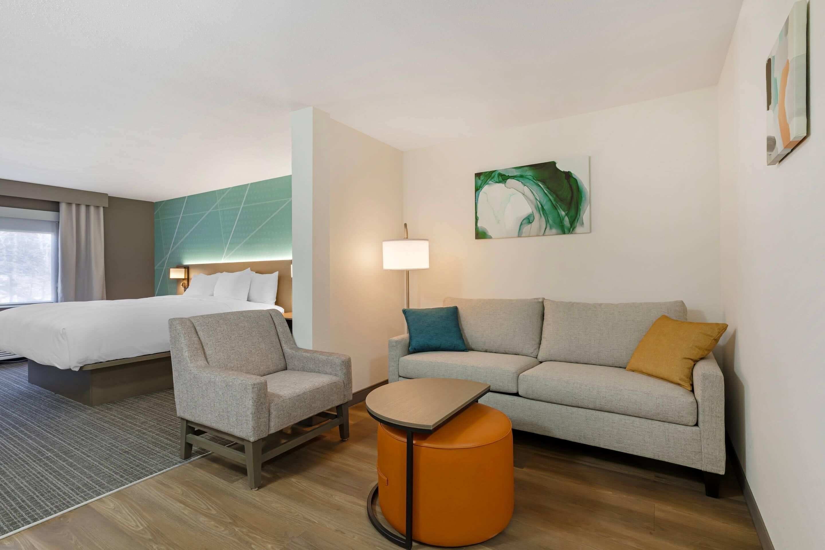 Una habitación de hotel con cama, sofá, sillón, una mesita y una lámpara.
