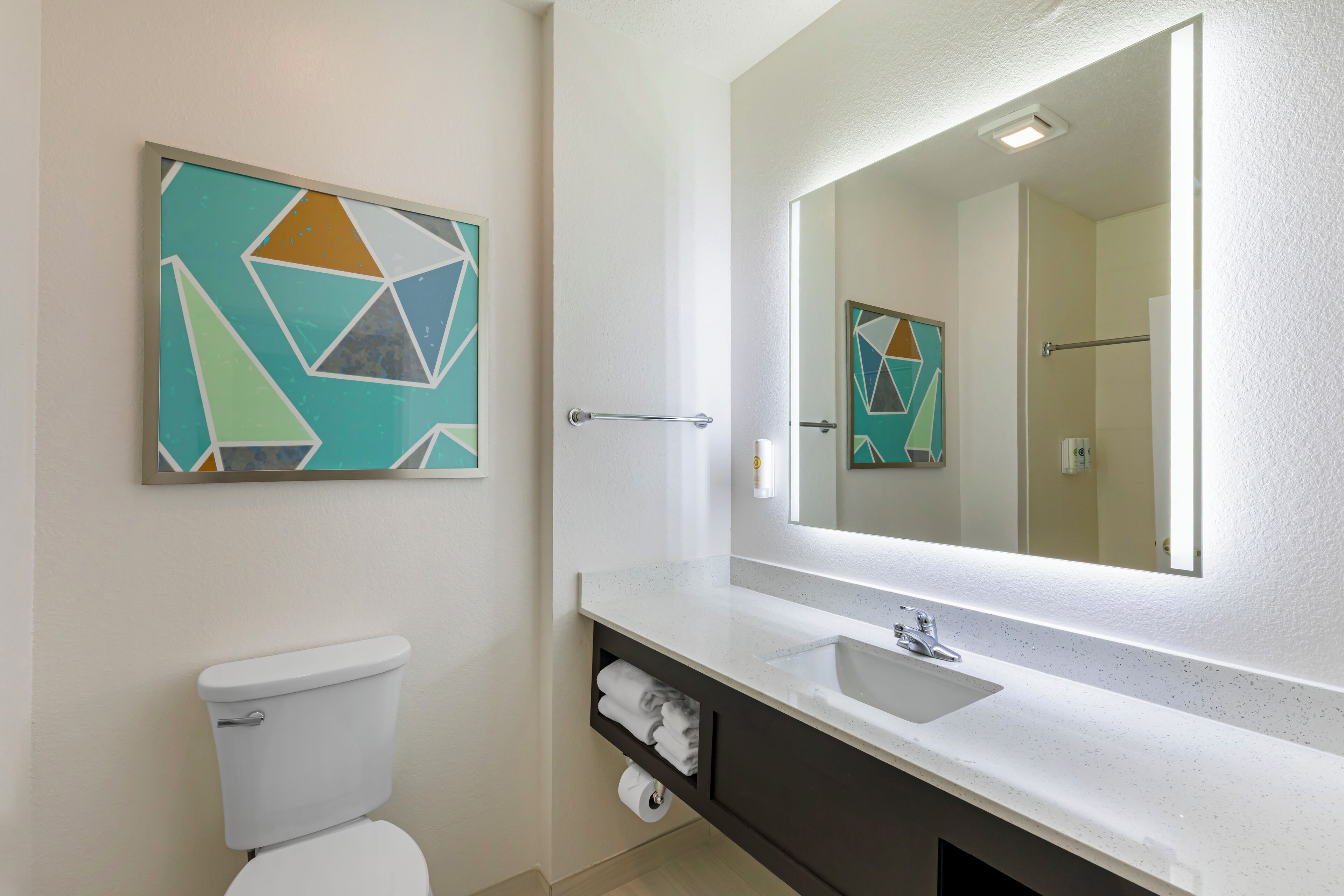 A modern bathroom with a toilet, sink, and mirror. There are geometric wall art pieces above the sink and toilet.