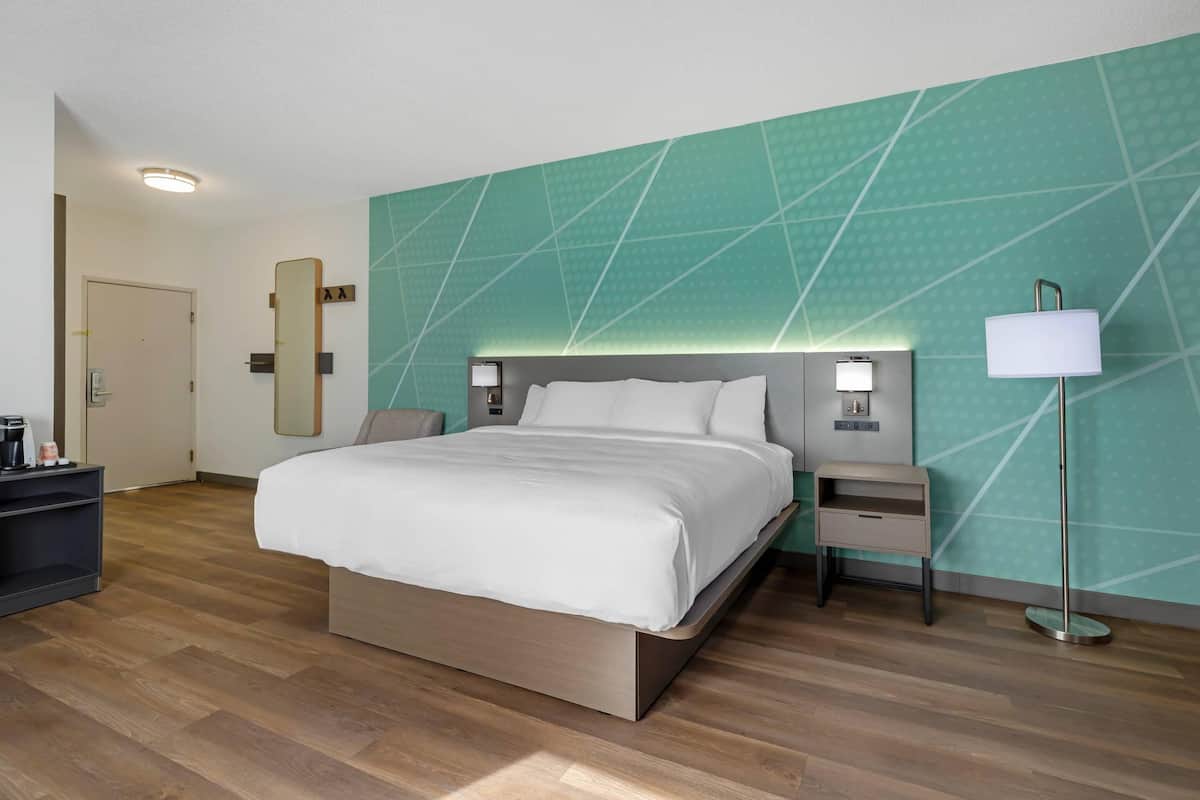 Una habitación de hotel con una cama grande, mesitas de noche, una lámpara de pie, un espejo y un armario.