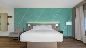 Une chambre d’hôtel avec un grand lit, une chaise, une table de chevet, une lampe et un miroir fixé au mur.