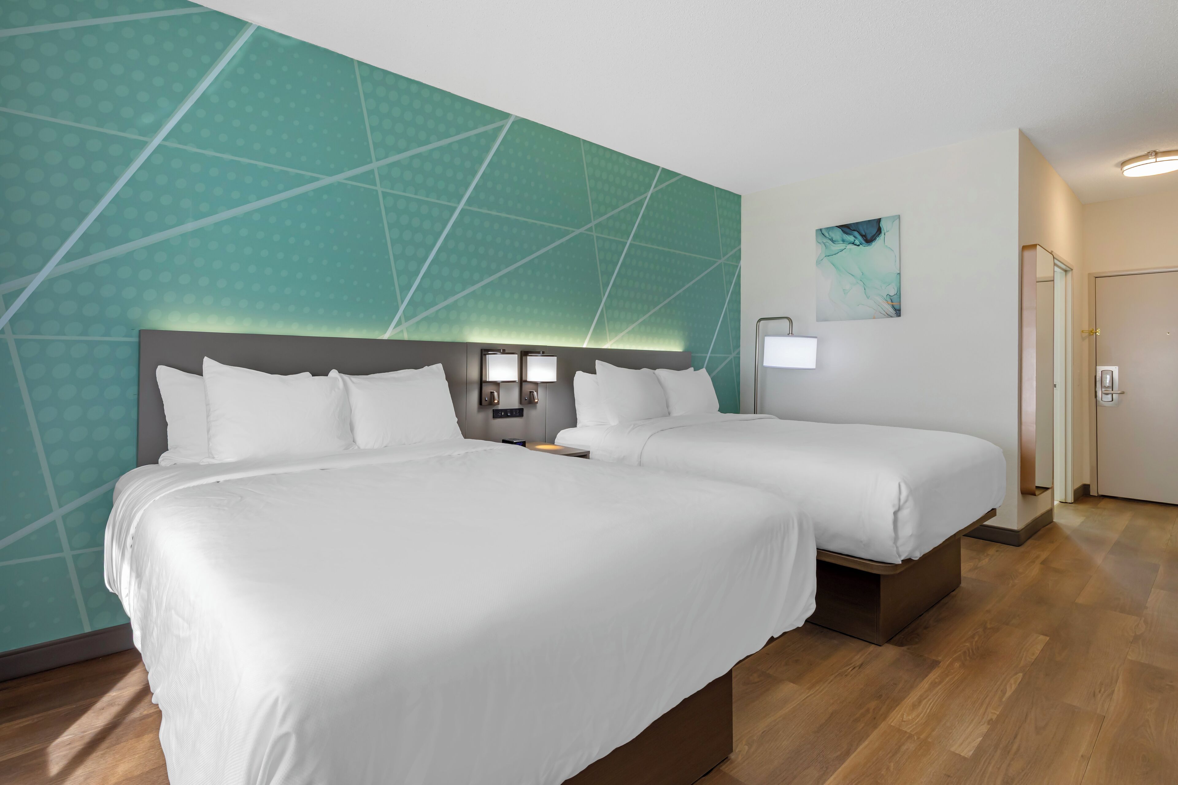 A hotel room with two beds, a teal accent wall, a modern light fixture, and a door.