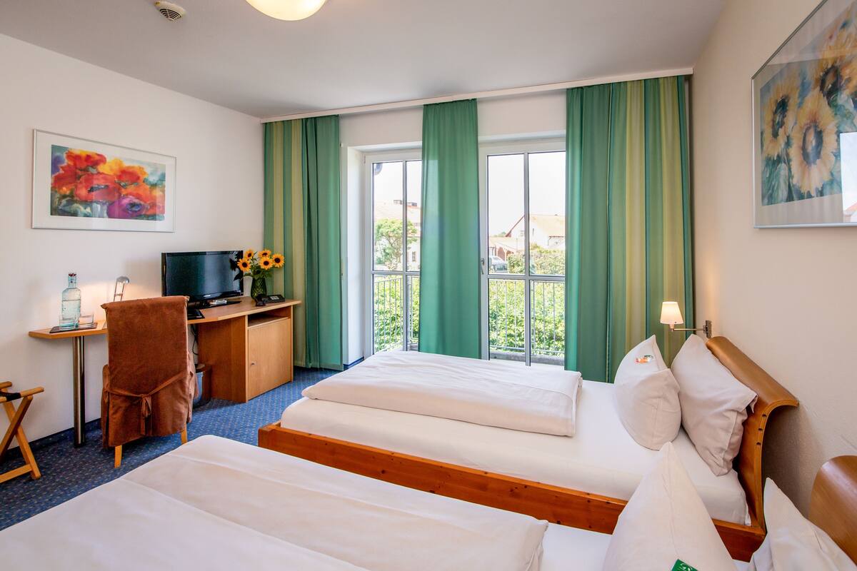 A hotel room with two beds, a desk with a computer, a chair, and a window with curtains.