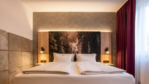 A large bed with white linens, two bedside tables with lamps, a large wall tapestry, and a red curtain. - ARCUS HOTEL MÜNCHEN MESSE (Vaterstetten)