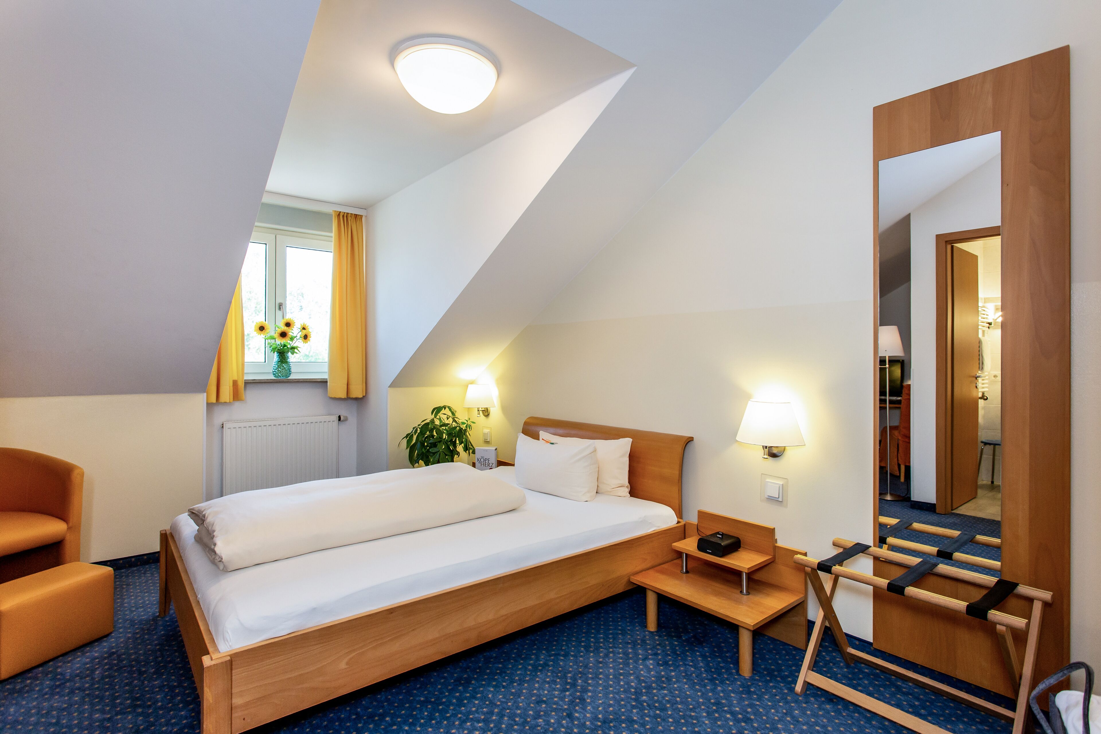 Una camera d'albergo con un letto, una scrivania, una sedia, uno specchio e una finestra con tende.