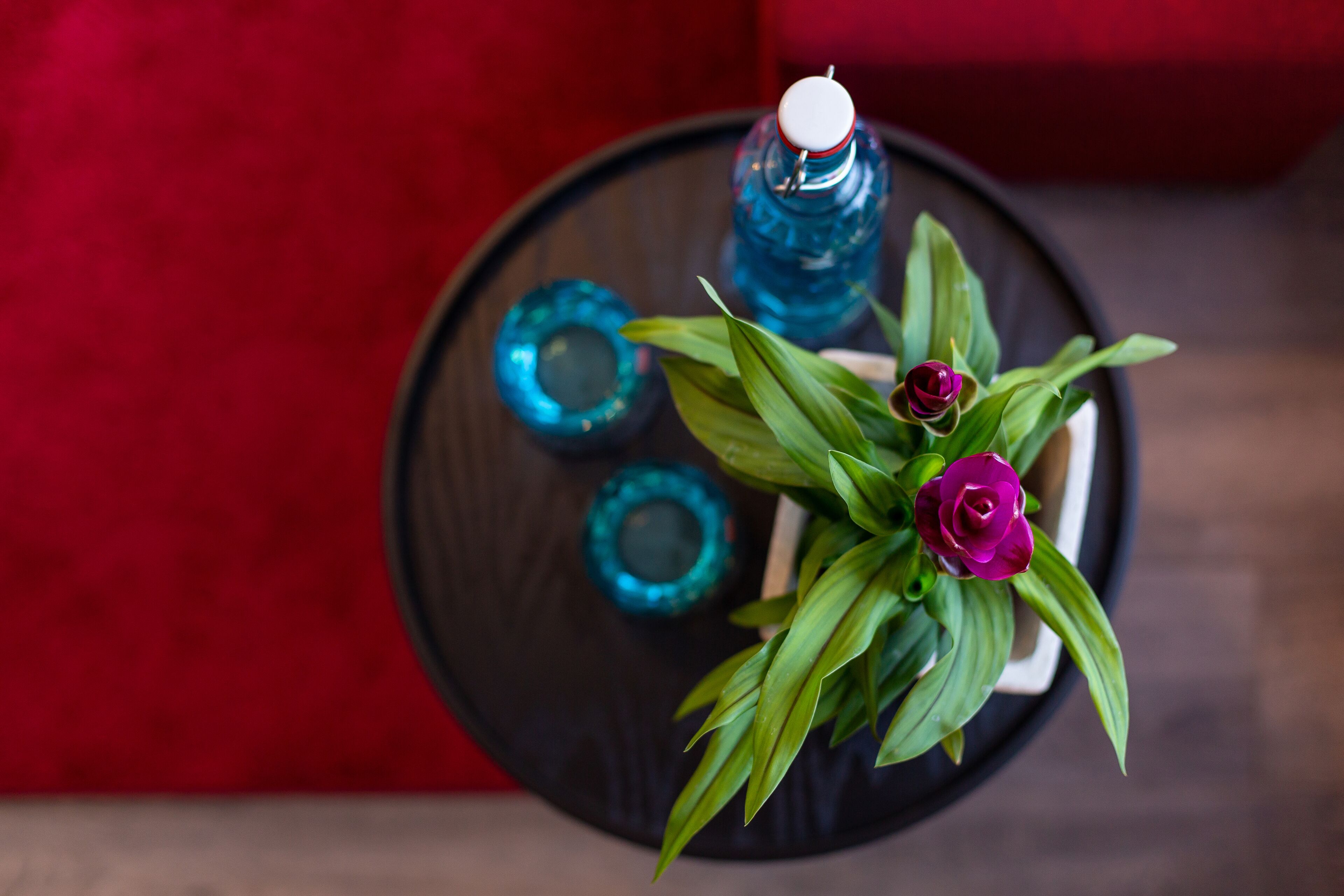 Una mesa redonda negra con una botella de agua azul, un vaso azul y una planta en maceta con hojas verdes y flores moradas.
