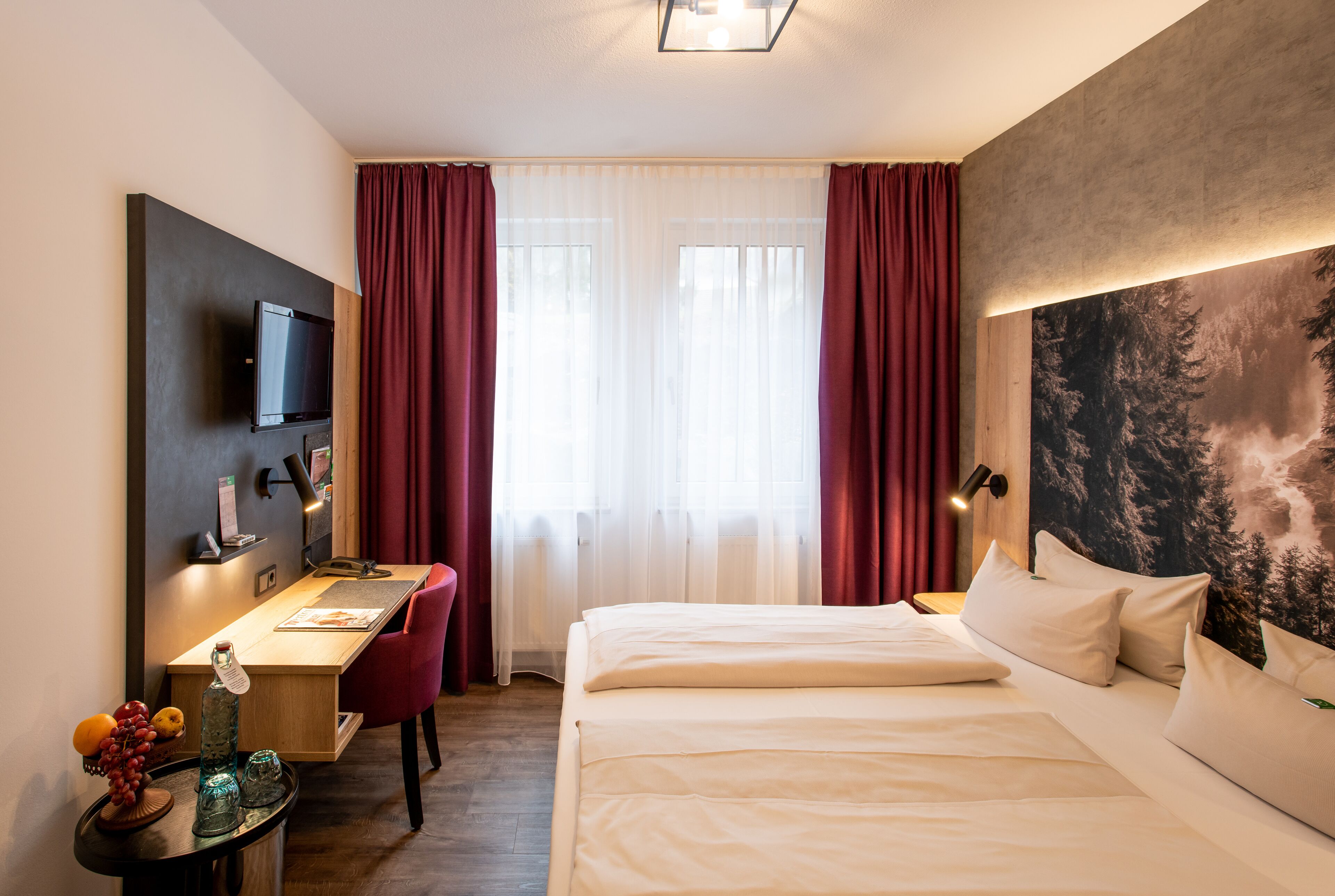 Een hotelkamer met een bed, een bureau, een stoel, een televisie en een groot schilderij aan de muur.