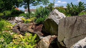 A garden with large rocks, ferns, and flowering plants. - ARCUS HOTEL MÜNCHEN MESSE (Vaterstetten)