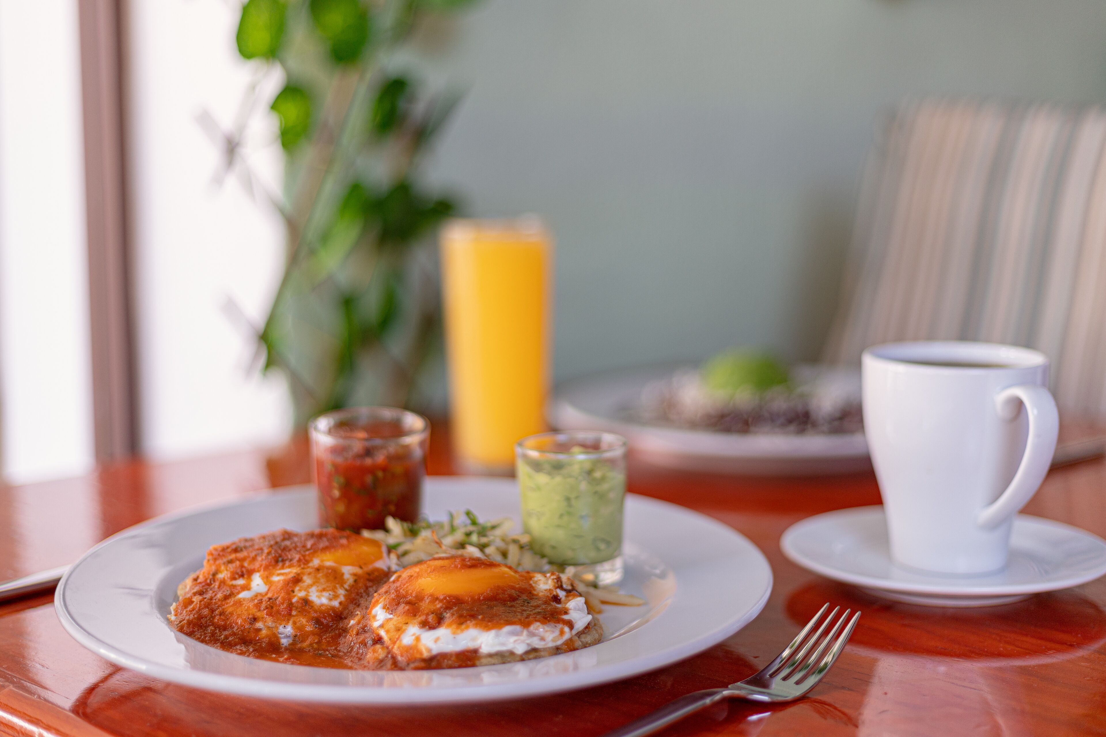 A breakfast setting with a plate of food, a cup, and a glass of juice on a wooden table.