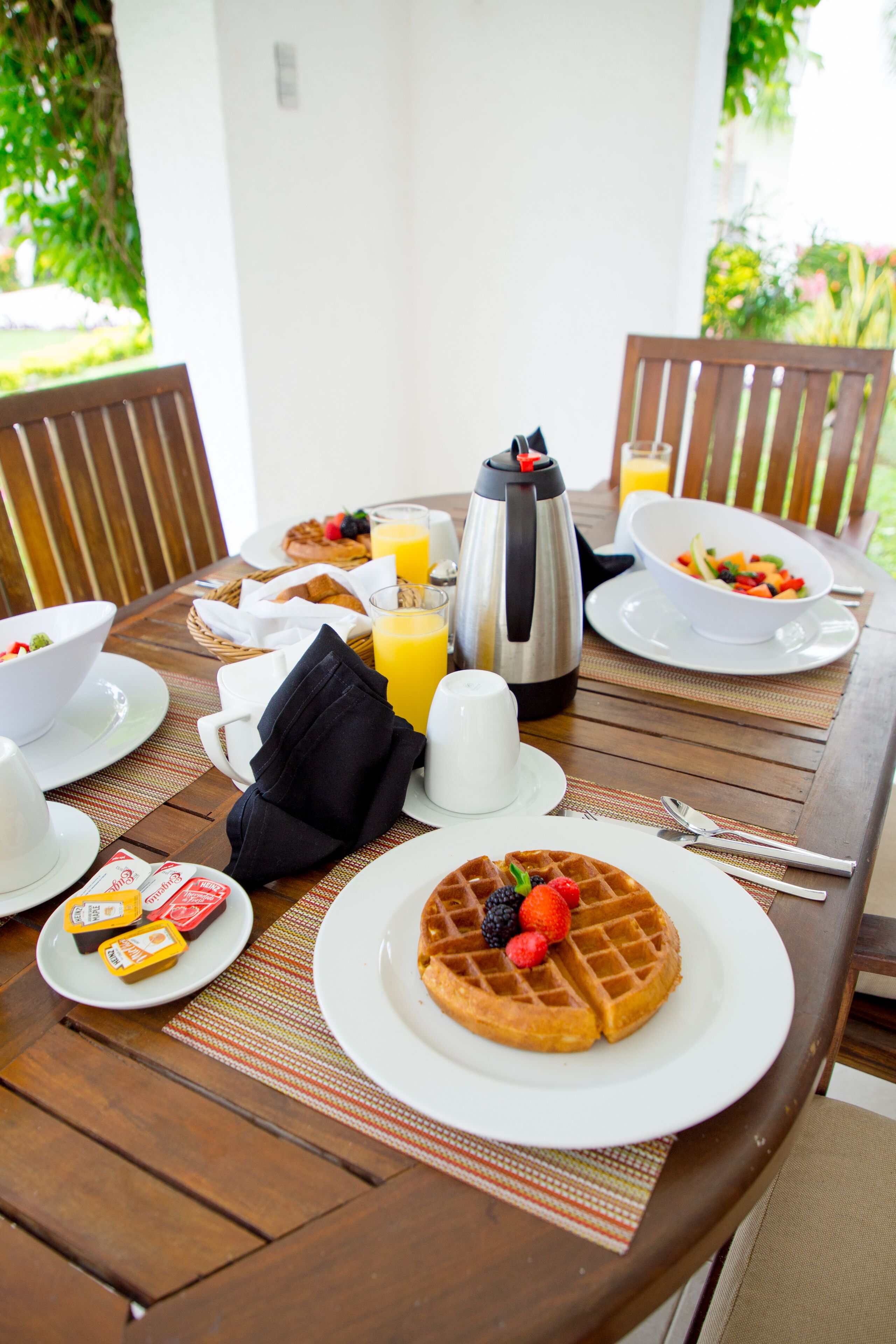 A breakfast table with waffles, fruit, coffee, and juice.