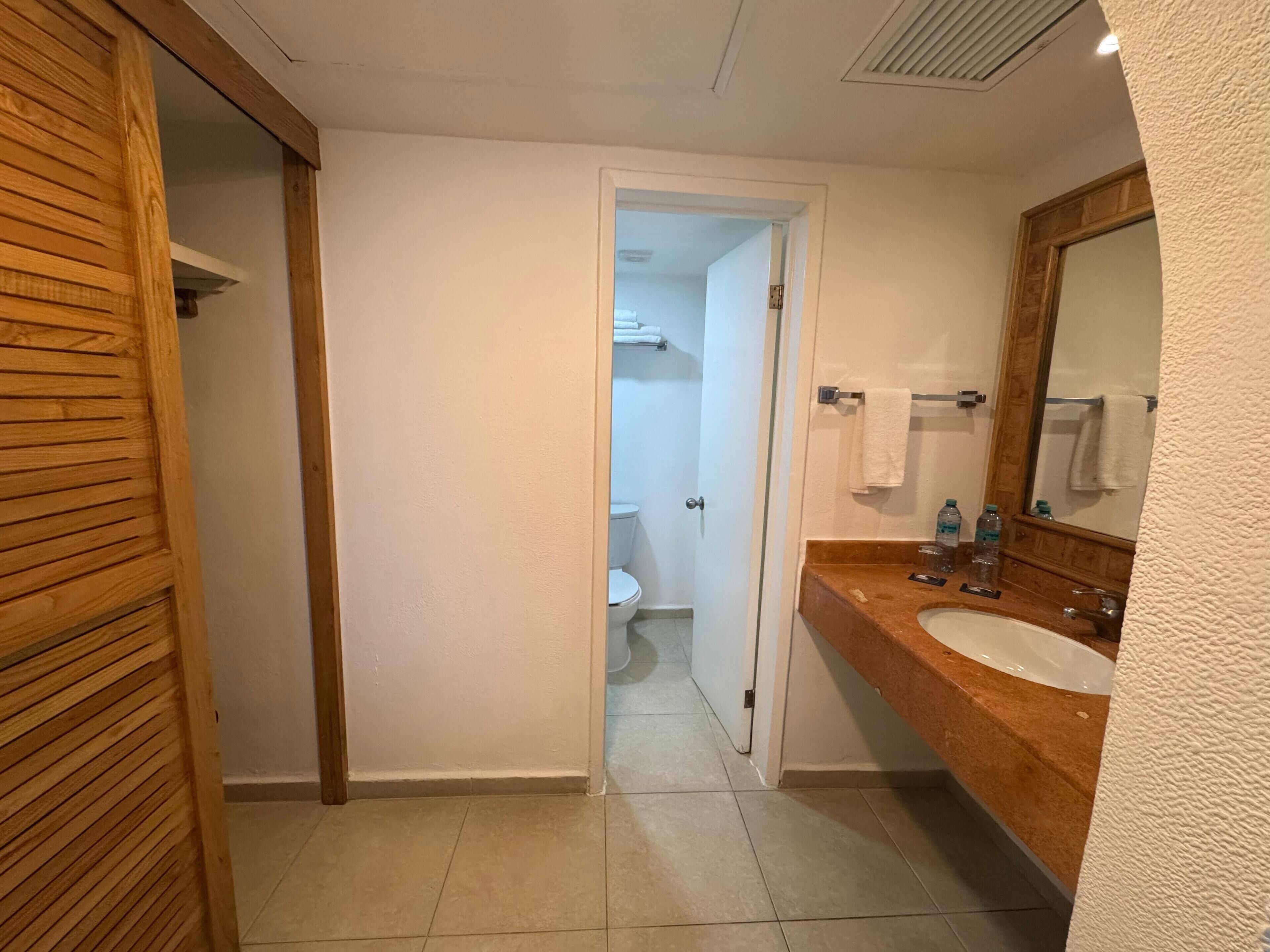 A bathroom with a wooden vanity, a sink, a mirror, and a toilet visible through an open door.