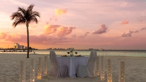 A beachside table set for two with a palm tree and city skyline in the background. - Beachscape Kin ha Villas & Suites (Cancun)