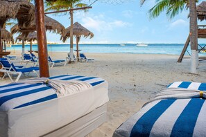 Relax on the beach with a clear view of the ocean from our lounge chairs under a thatched roof.
