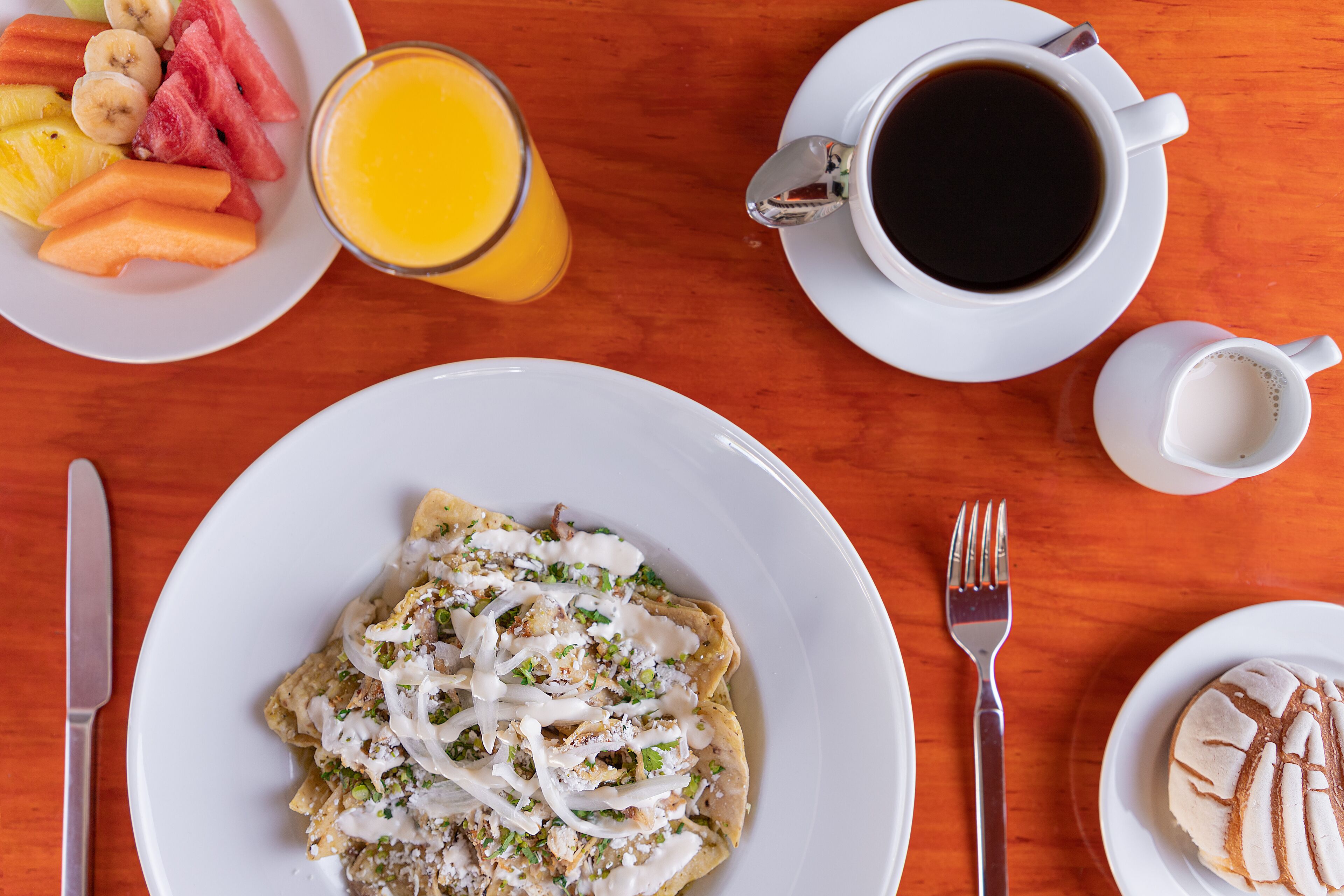Een ontbijttafel met een bord nachos, een glas jus d'orange en een kop koffie.