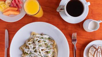 A breakfast setting with a plate of nachos, a glass of orange juice, and a cup of coffee on a wooden table.