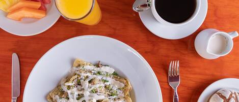 Een ontbijttafel met een bord nachos, een glas jus d'orange en een kop koffie.