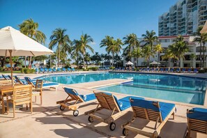 Relax by the resort pool surrounded by palm trees and lounge chairs.