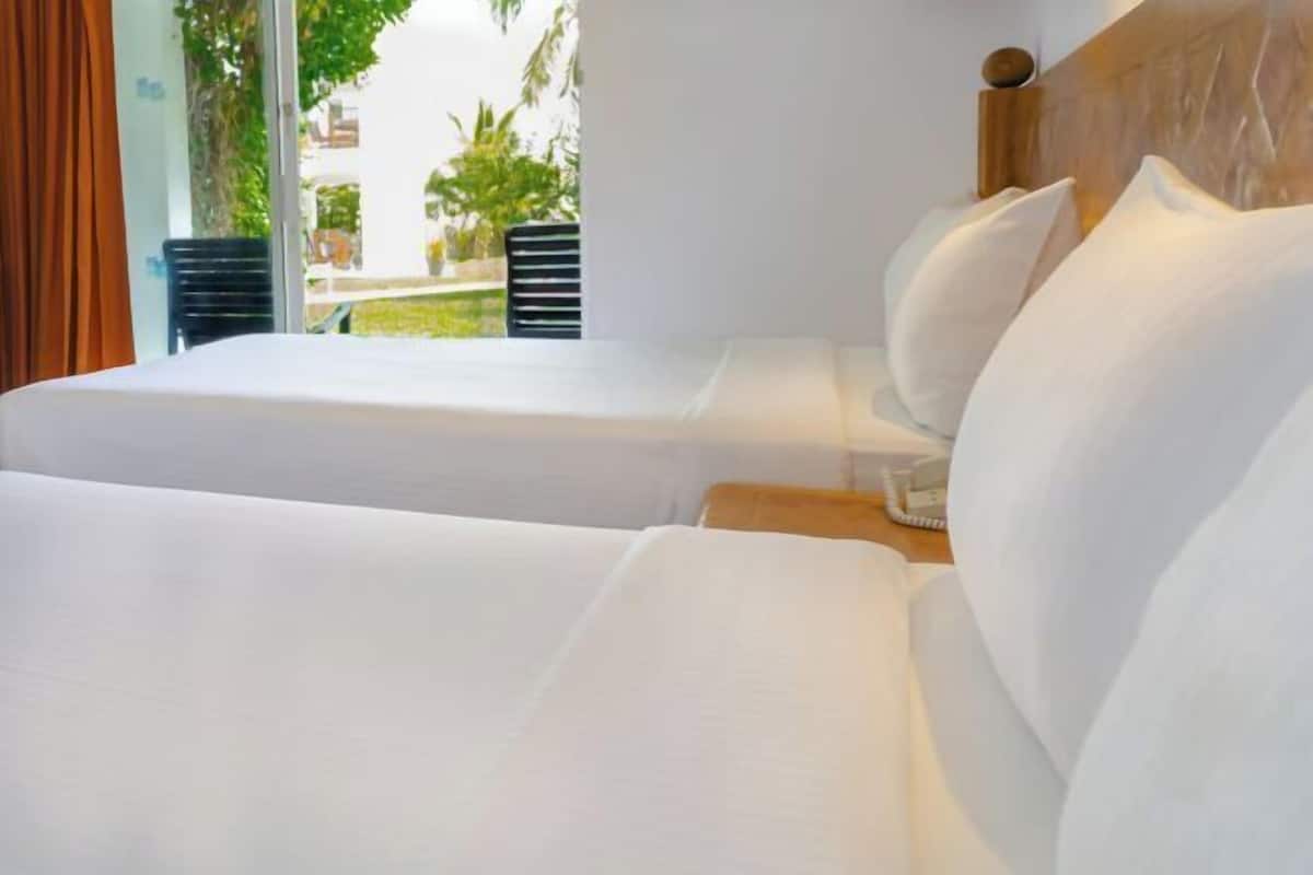 A hotel room with two beds, a wooden headboard, and a view of greenery outside.