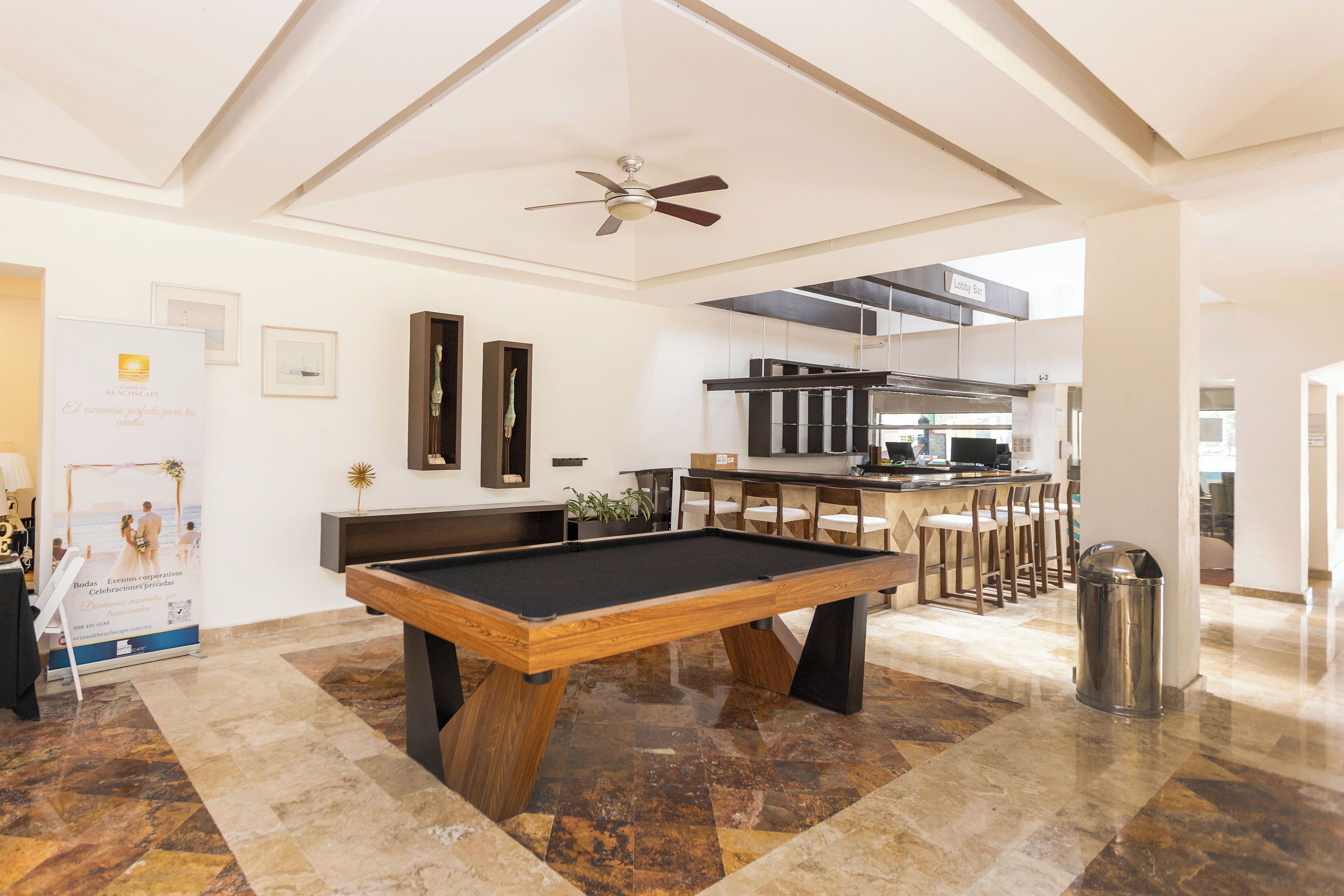 A pool table in a spacious room with a ceiling fan, a kitchen area, and a bar.