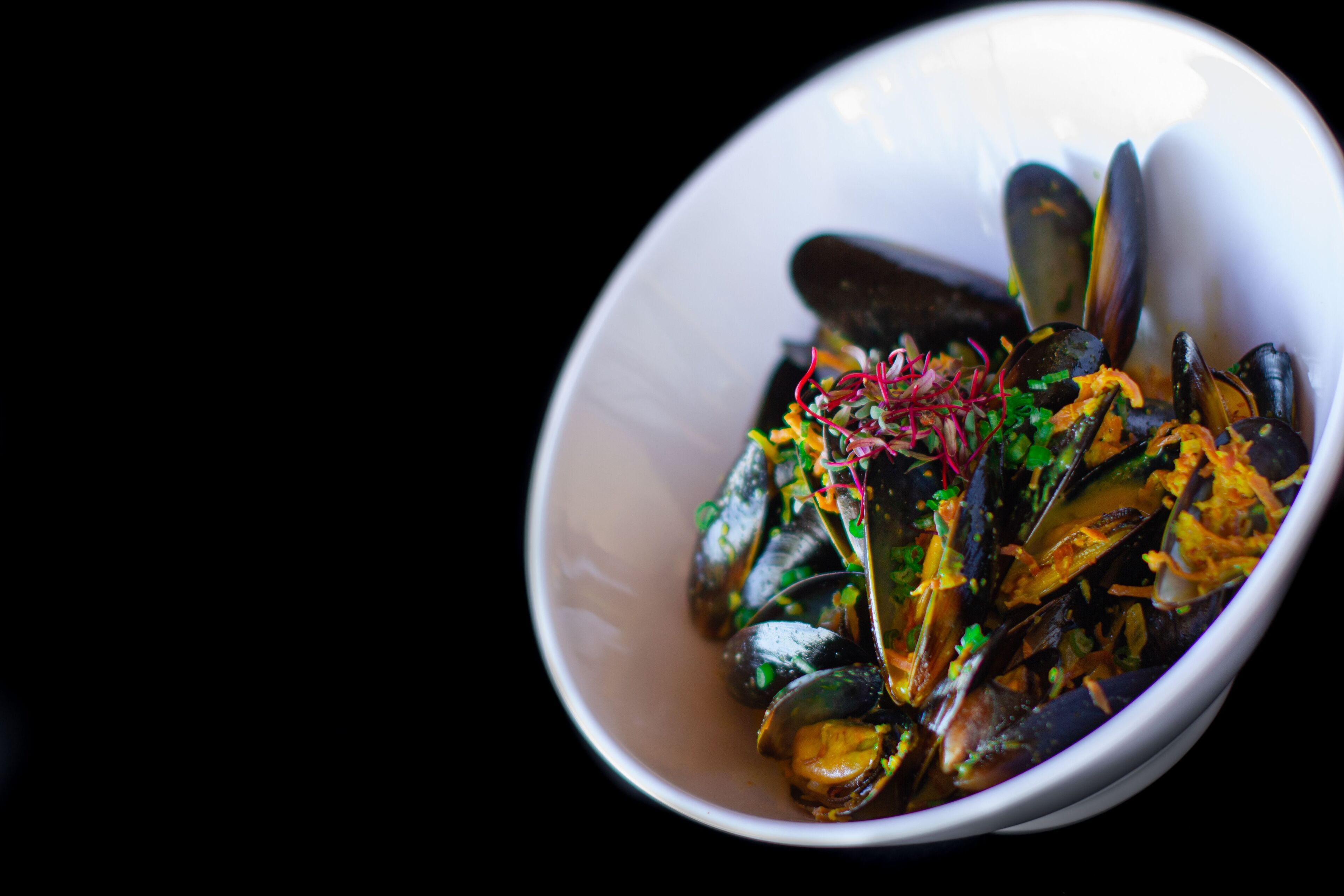 A white bowl containing mussels garnished with herbs and shredded vegetables.