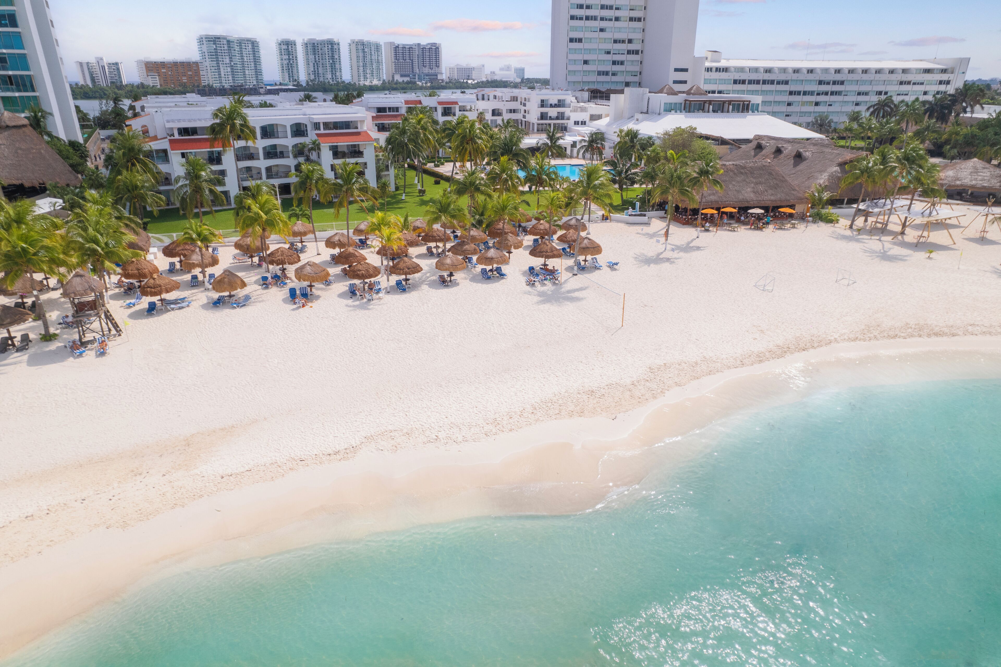 A beach resort with thatched umbrellas, sun loungers, and a pool area.