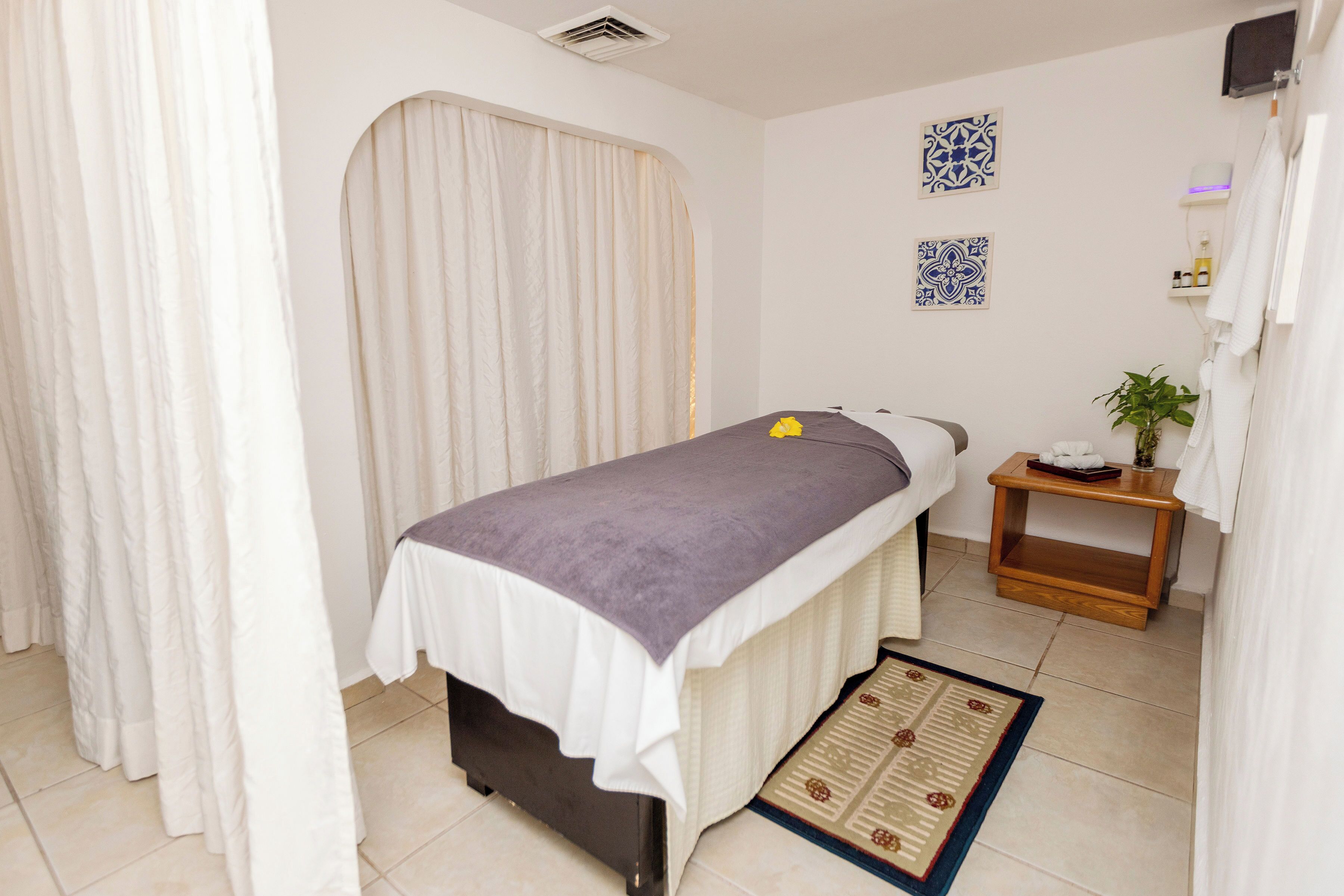 A room with a bed, a small bedside table, a wall-mounted air conditioner, and a wall-mounted shelf with a plant.