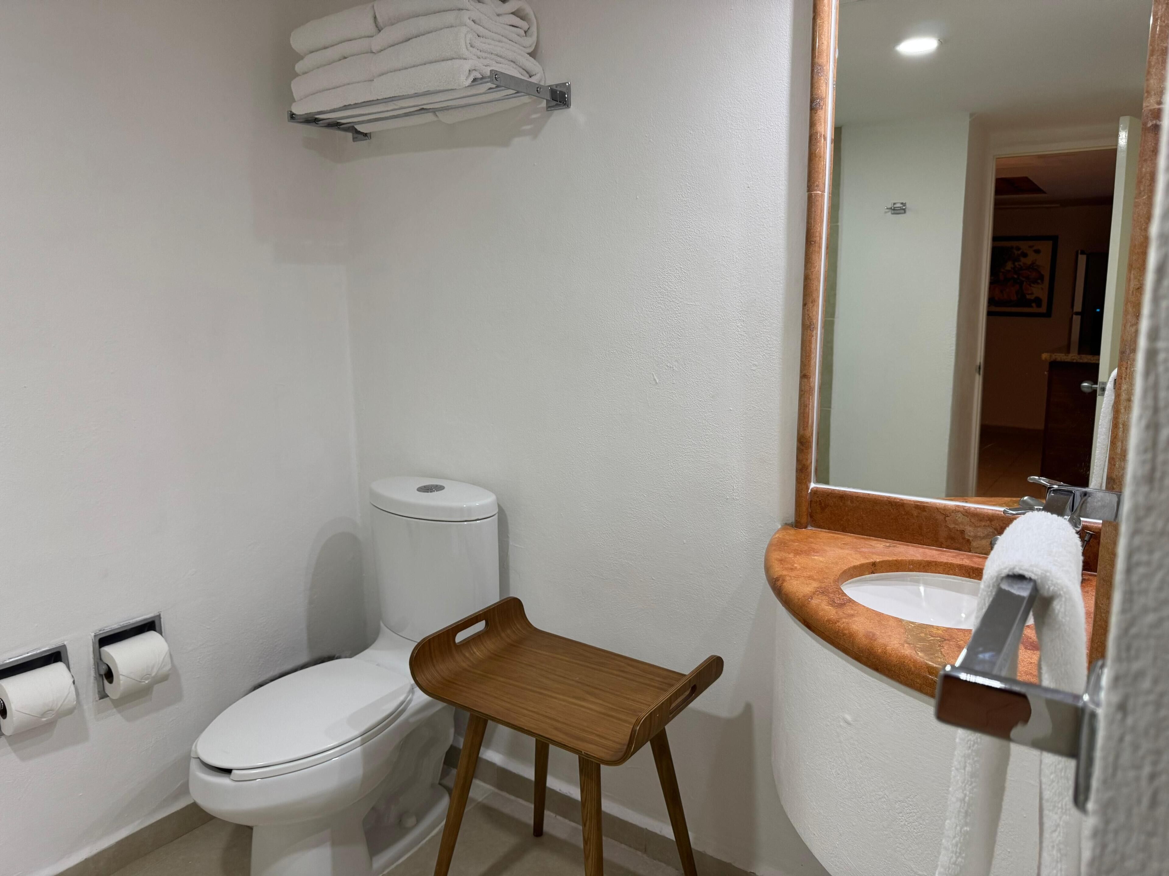 A bathroom with a toilet, a sink with a wooden tray, and a towel rack.
