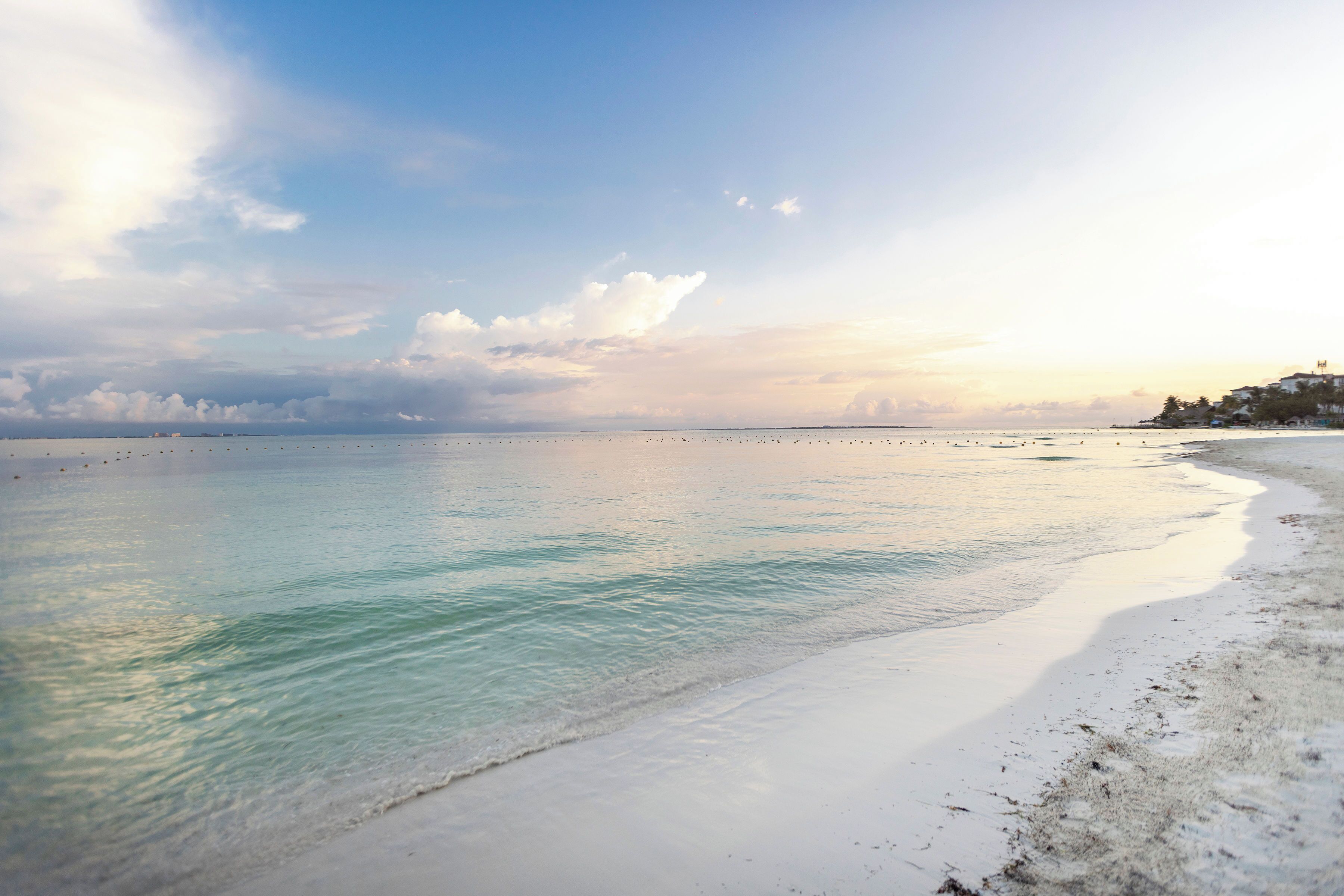 A beach with clear water, a sandy shore, and a distant shoreline with buildings.